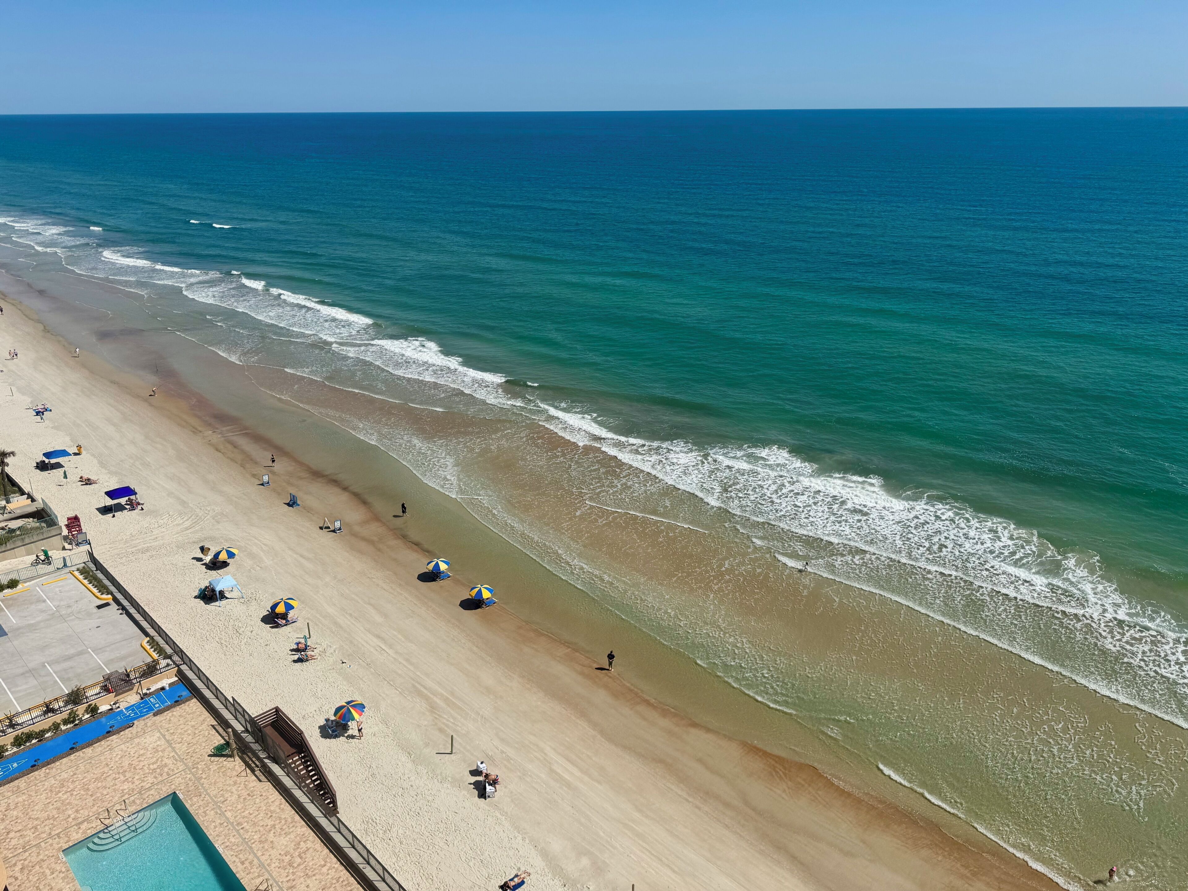 A beach with a swimming pool, umbrellas, and a lifeguard tower.