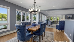 A dining area with a wooden table, blue upholstered chairs, and a chandelier. - Oasis on Murray Lake, just NE of Grand Rapids (Lowell)