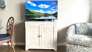 Ein Fernseher auf einem Schrank, ein Sessel und eine gepolsterte Couch in einem Zimmer.