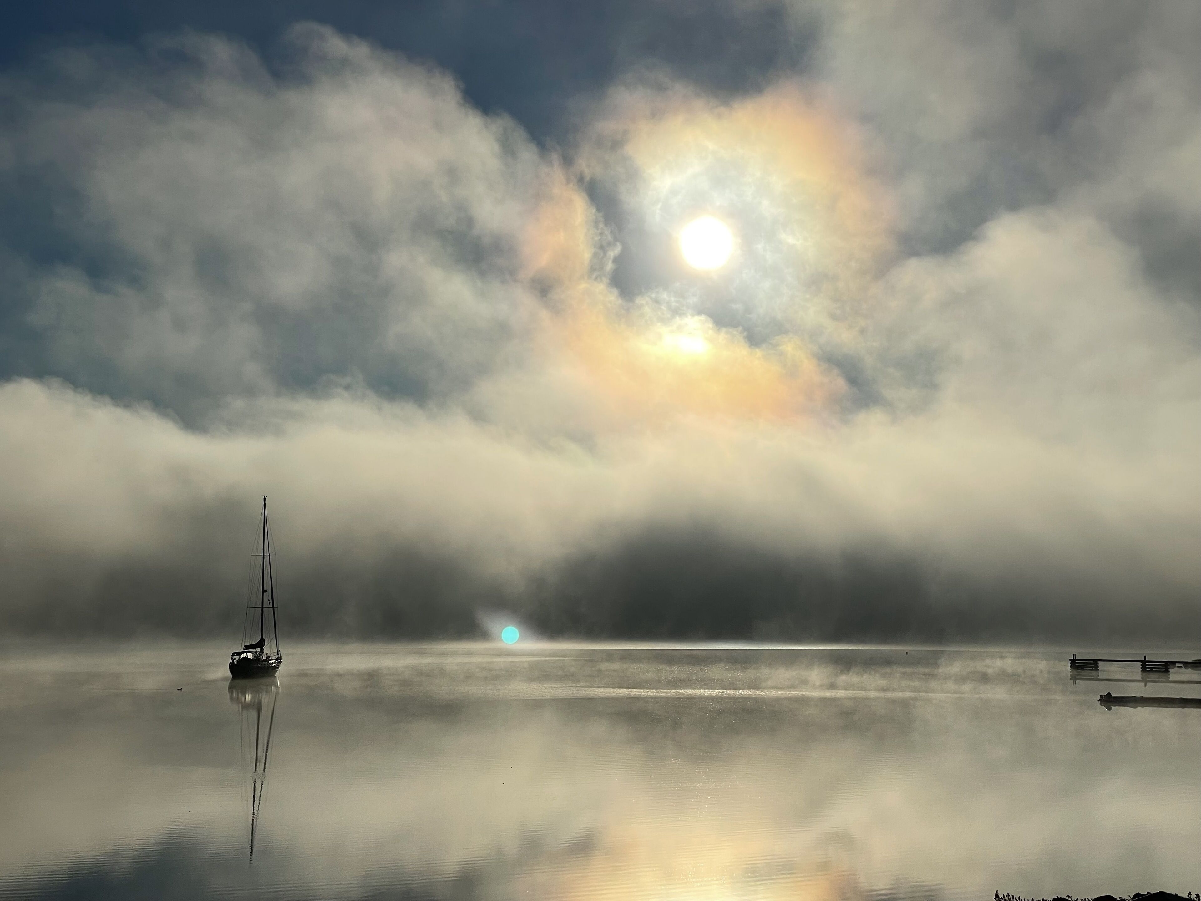A calm lake with a sailboat and a dock.