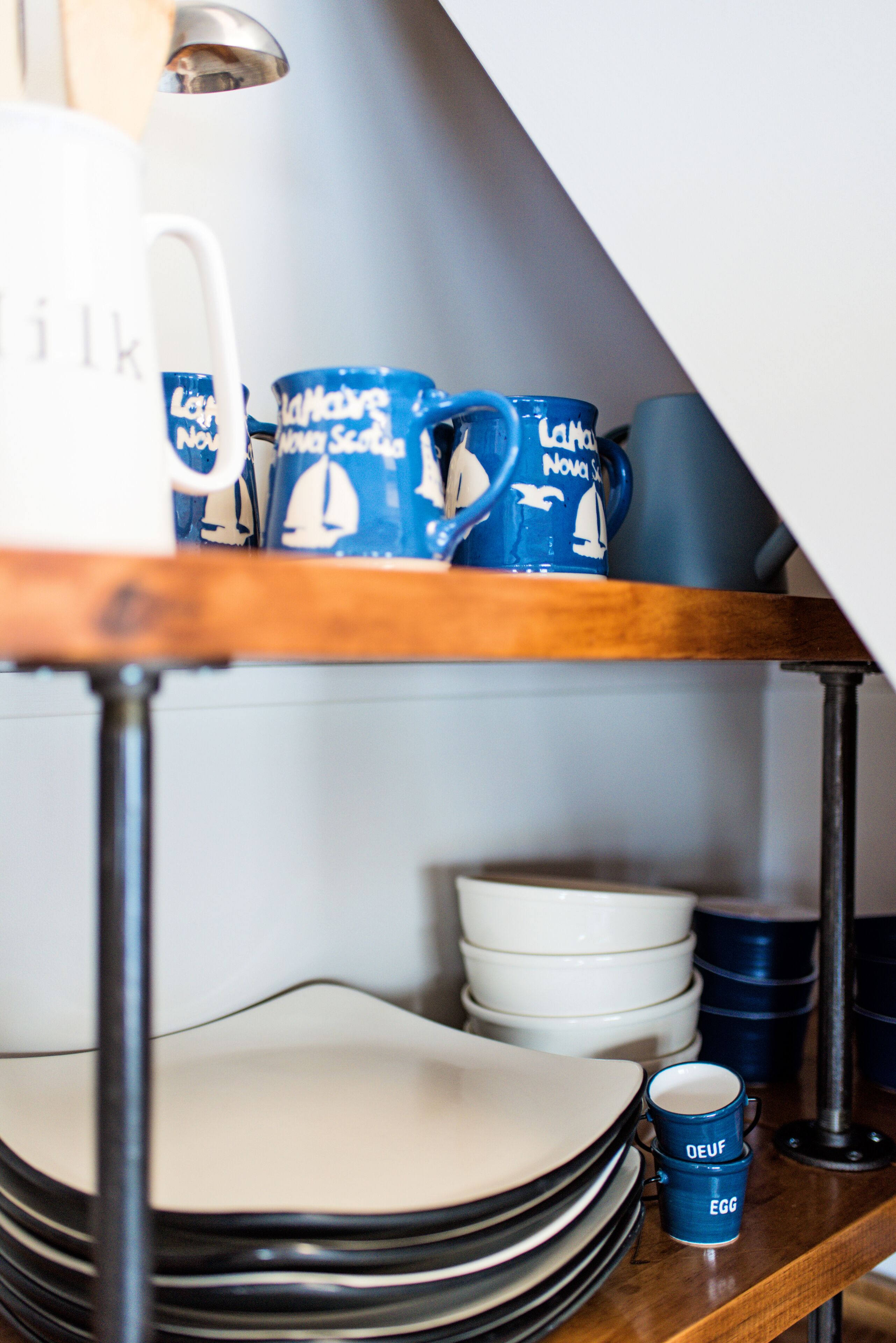 A shelf with stacked plates and blue mugs with sailboat designs.