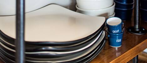 A shelf with stacked plates and blue mugs with sailboat designs.