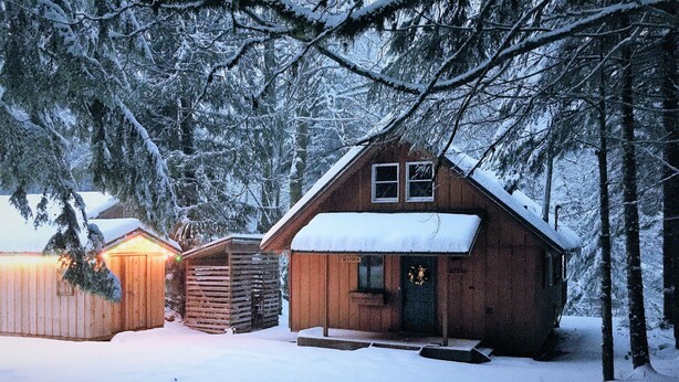 A wooden cabin with a snow-covered roof and a porch, surrounded by trees. - Cozy Riverfront Cabin Near Crystal Mountain & Sunrise Mt. Rainier National Park (Greenwater)