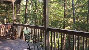 A wooden deck with a rocking chair and a log. - Cozy Riverfront Cabin Near Crystal Mountain & Sunrise Mt. Rainier National Park (Greenwater)