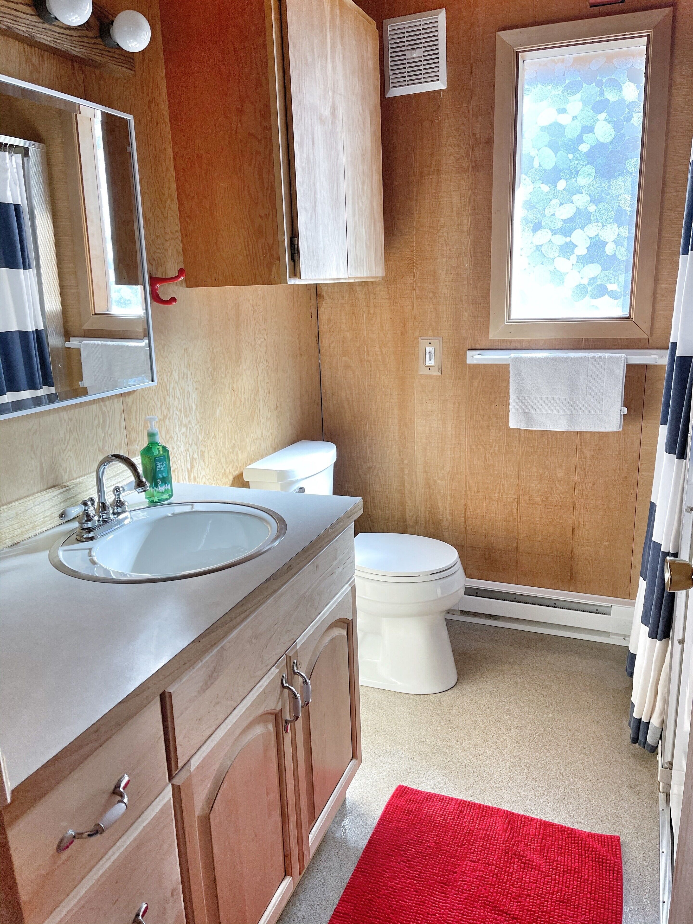 A compact bathroom with a wooden vanity, a sink, a toilet, and a window with a view of bubbles.