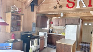 A kitchen with wooden cabinets, a stove, and a refrigerator. There is a wooden ceiling with a ski-themed decoration. - Cozy Riverfront Cabin Near Crystal Mountain & Sunrise Mt. Rainier National Park (Greenwater)