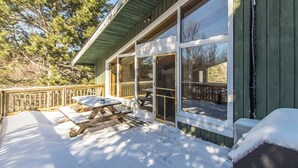 A wooden deck with picnic tables and a covered area, surrounded by snow.