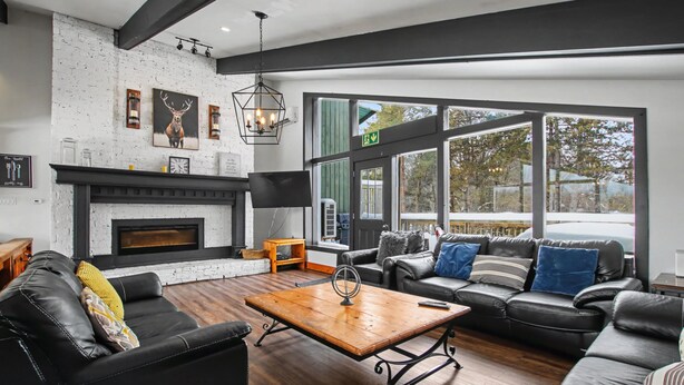 A modern living room with a fireplace, leather sofas, a coffee table, and large windows offering a view of the outdoors.