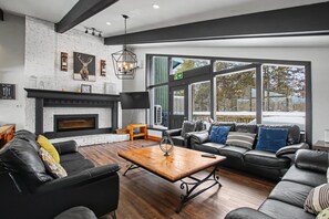 A modern living room with a fireplace, leather sofas, a coffee table, and large windows offering a view of the outdoors. - Mountain Trail Blue Mountain (The Blue Mountains)