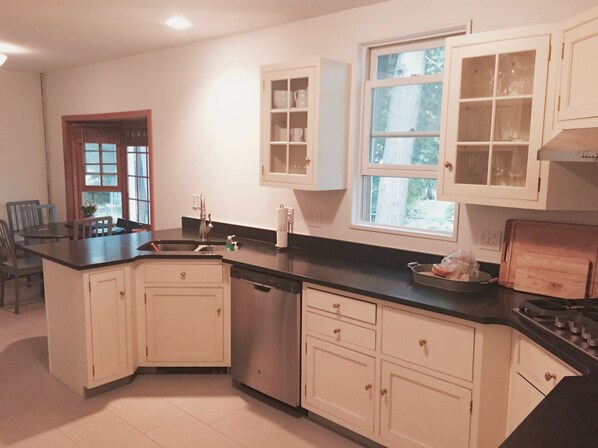 A kitchen with white cabinets, a black countertop, a window, and a dining area with chairs.