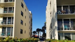Um caminho entre dois edifícios com varandas, rodeado por vegetação.