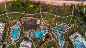 Luftaufnahme eines Resorts mit mehreren Schwimmbecken, einem großen Gebäude und einem Strand.