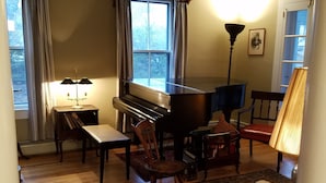 Ein Wohnzimmer mit einem Flügel, einem Tisch, Stühlen, einer Lampe und einem Teppich.