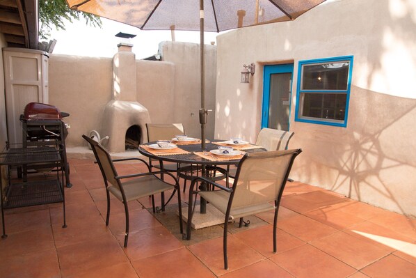 Un patio con una mesa redonda, sillas y una parrilla.