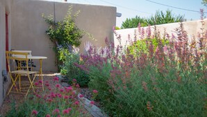 En have med et træbord, stole, en støbt mur og forskellige blomstrende planter.