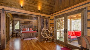 Ein rustikales Blockhaus mit Holzboden, einem Bett mit roter Bettwäsche, einem großen Holzrad und einer roten Couch auf einem Balkon.