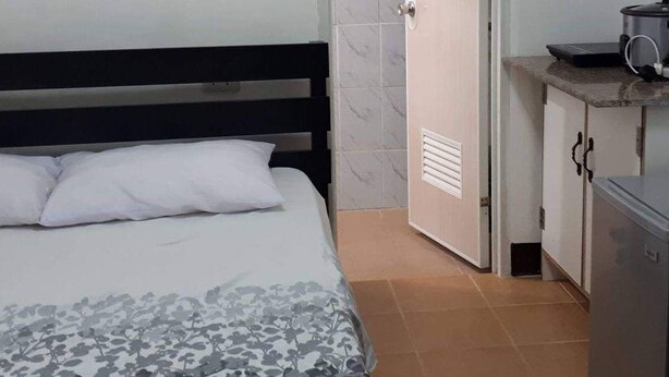 Une chambre comprenant un lit, une table de chevet, une petite kitchenette équipée d’un four à micro-ondes et une salle de bain avec douche.