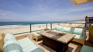 Un balcone con tavolo in pietra e sedute imbottite color verde chiaro, con vista su una spiaggia con persone e ombrelloni.