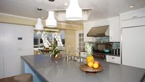 Una cucina moderna con mobili bianchi, un piano di lavoro in granito e un'isola centrale con frutta e fiori.