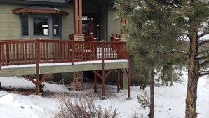 A wooden deck with a stone pillar, a covered porch, and a snow-covered landscape. - Spacious High Country Custom Home with Stunning Views (Williams)