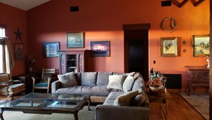 A living room with a large sofa, a glass coffee table, and a fireplace. There are framed pictures on the walls and a star decoration on the ceiling. - Spacious High Country Custom Home with Stunning Views (Williams)