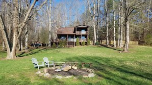 Une cabane à deux étages avec une terrasse, entourée d’arbres et d’une pelouse.