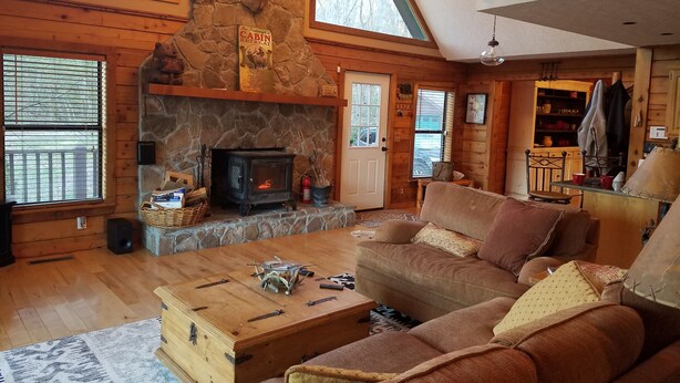 L’intérieur chaleureux d’un chalet avec une cheminée en pierre, des meubles en bois et une grande fenêtre donnant sur le paysage extérieur.