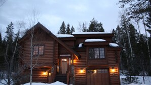 En hytte med træfacade, veranda og et tag dækket af sne.