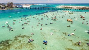 An aerial view of a coastal area with numerous boats, a pier, and a resort in the background.
