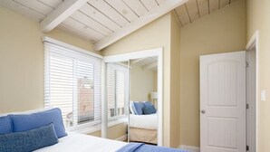 Ein Schlafzimmer mit einem Bett, einem Fenster mit Jalousien, einer Tür und einem Spiegel, der das Bett wiederspiegelt.