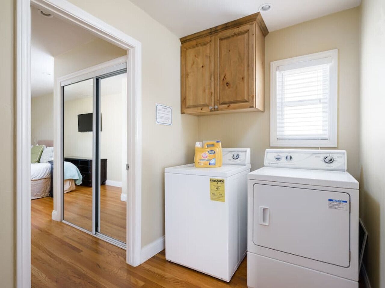 A laundry room with two white washing machines, one with a detergent bottle on top.