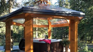 Een houten prieel met een jacuzzi, omringd door een terras en een tuin.