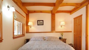 Een slaapkamer met een groot bed, twee bedlampen, een lijst met een afbeelding aan de muur en een houten deur.