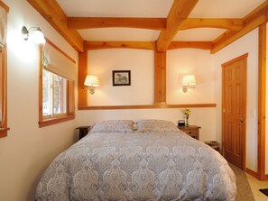 Ein Schlafzimmer mit einem großen Bett, zwei Nachttischlampen, einem gerahmten Bild an der Wand und einer Holztür.