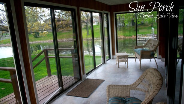 A sun porch with wicker furniture, a view of a lake, and a wooden deck.