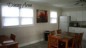 A dining area with a wooden table and chairs, a refrigerator, a microwave, and a painting on the wall.