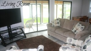 A living room with a sofa, armchair, and TV stand.