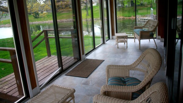 A sun porch with wicker furniture, a view of a lake, and a wooden deck.