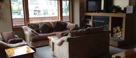 A cozy living room with a sofa, two wooden chairs, a small table, a fireplace, and a television.