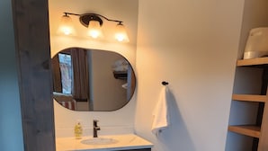 Ein Schlafzimmer mit einem Bett, einem runden Spiegel, einem Waschbecken und einem Holzbodenregal.