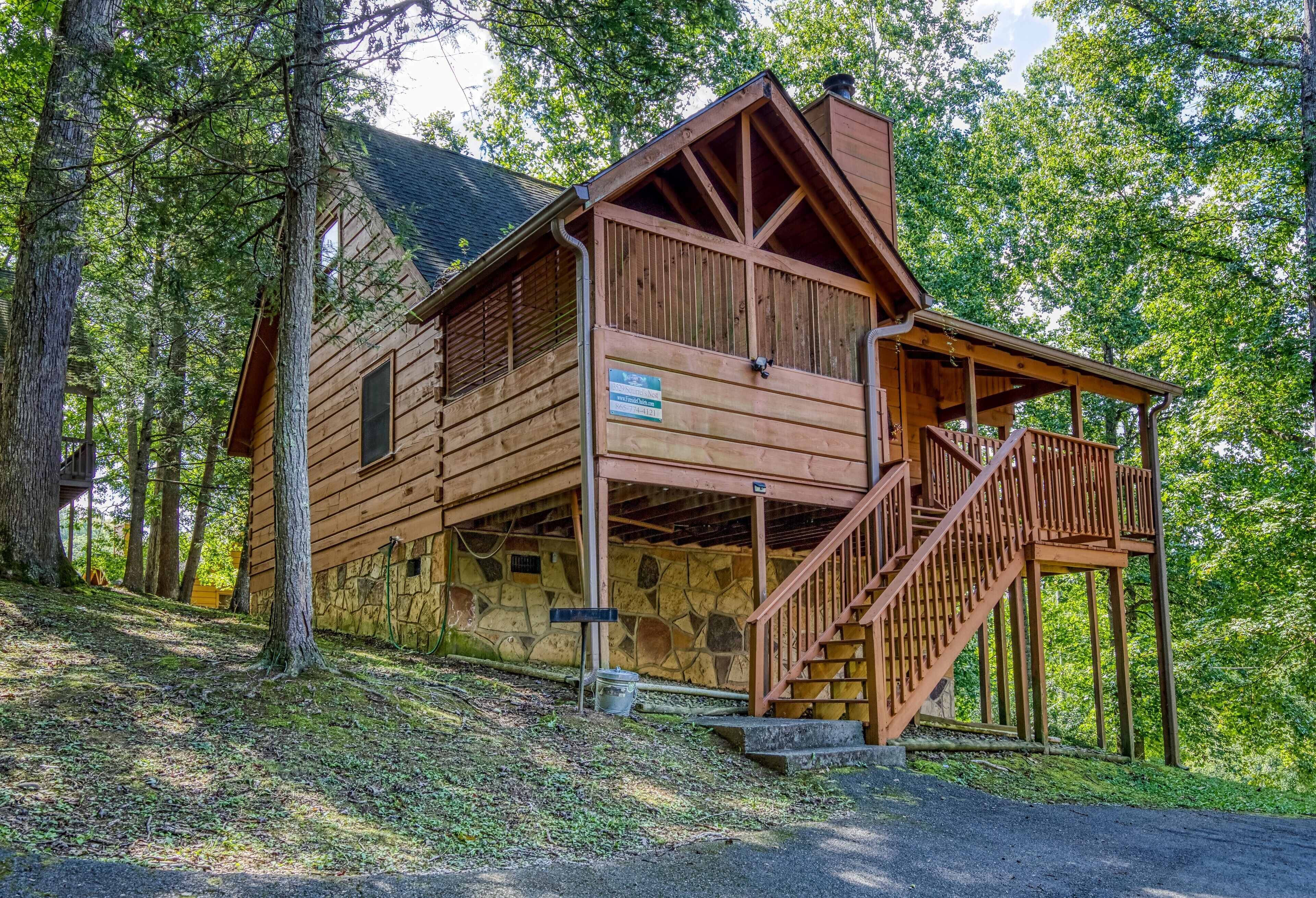 A wooden cabin with a stone foundation, a wooden porch, and a staircase leading to a deck.