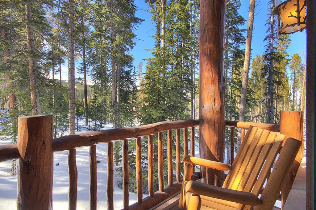 A wooden deck with a bench, surrounded by tall pine trees and a clear sky.