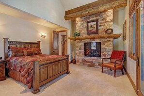 Un dormitorio con una cama grande, una chimenea de piedra y una silla de madera.