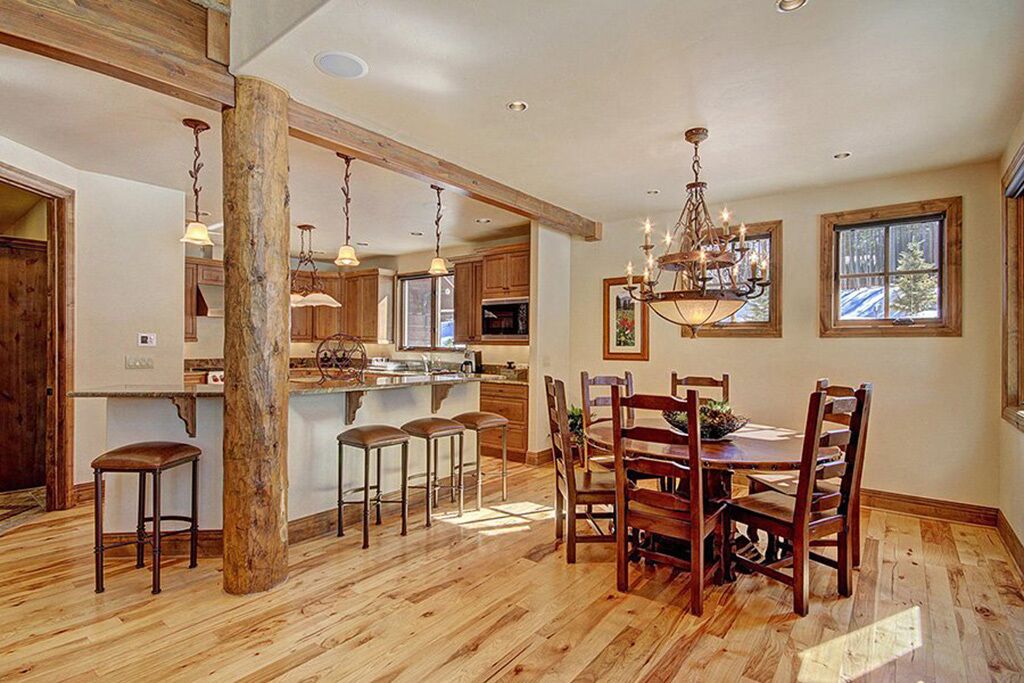 A spacious kitchen with wooden beams, a central island with bar stools, and a chandelier.