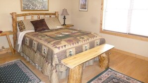 A bedroom with a wooden bed, a bench, a lamp, and two framed pictures on the wall. - Laramie Bluffs Mountain Getaway (Custer)