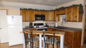 A kitchen with wooden cabinets, a white refrigerator, a microwave, a stove, and a bar area with stools. - Laramie Bluffs Mountain Getaway (Custer)