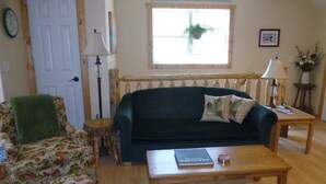A cozy living room with a green sofa, a patterned armchair, a wooden coffee table, and a small side table. - Laramie Bluffs Mountain Getaway (Custer)