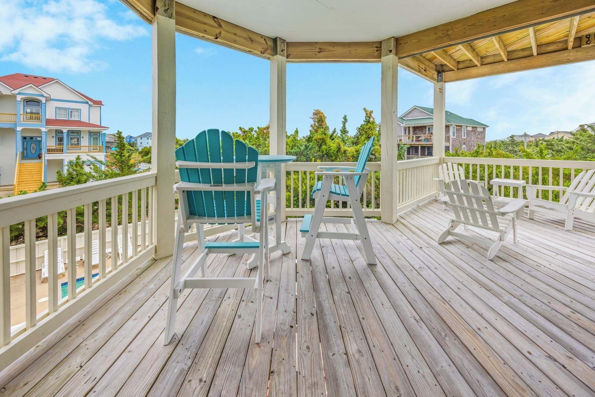 A wooden deck with white railings and blue Adirondack chairs.
