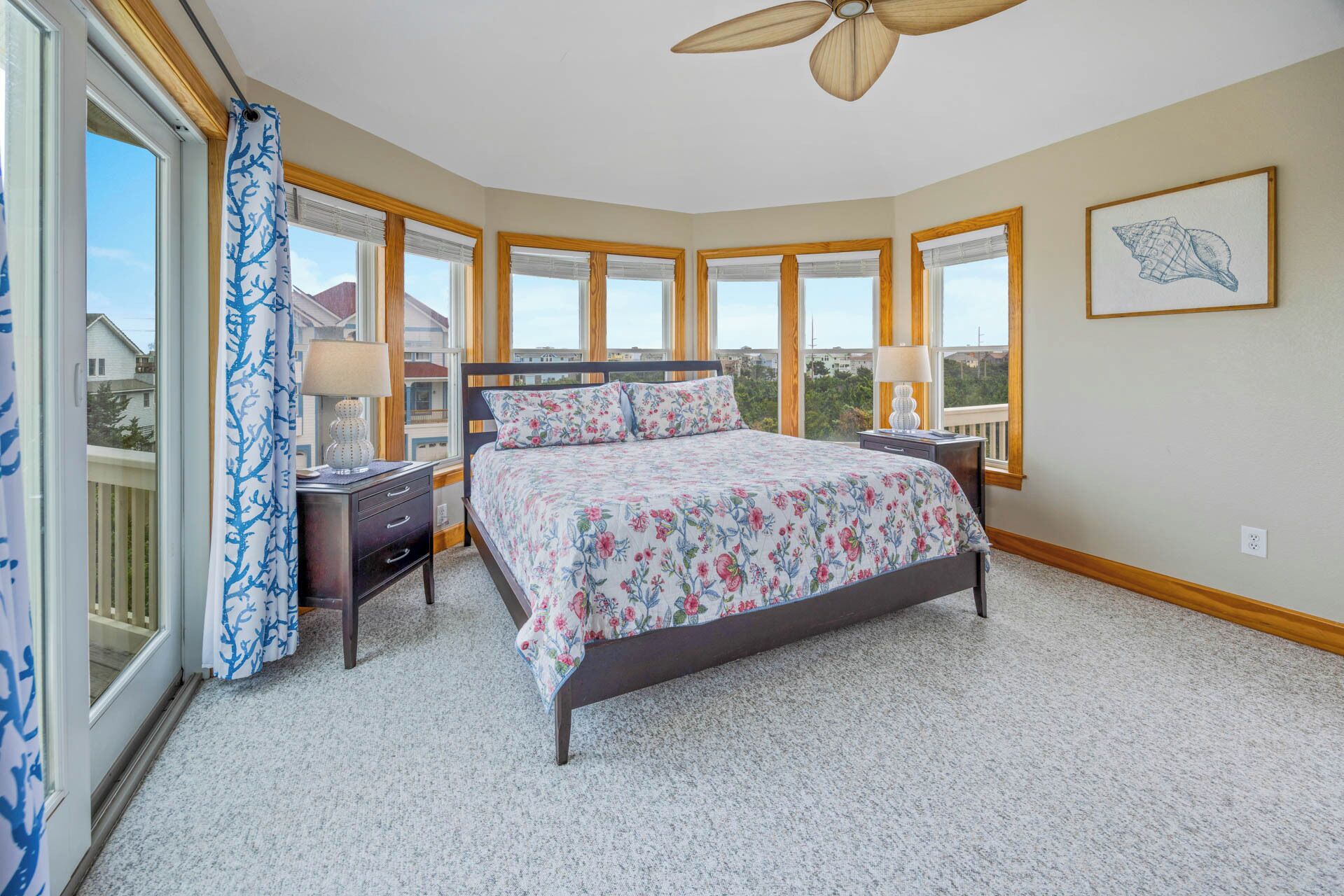 A bedroom with a large bed, two bedside tables, a ceiling fan, and a window with a view of the outside.
