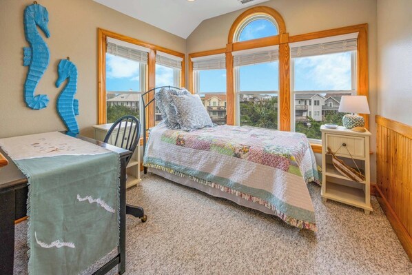 A bedroom with a bed, a desk, and a chair. There are large windows with a view of houses. - Soundside Home with Private Pool, Hot Tub, Game Room, Home Theaters, Tiki Bar (Avon)